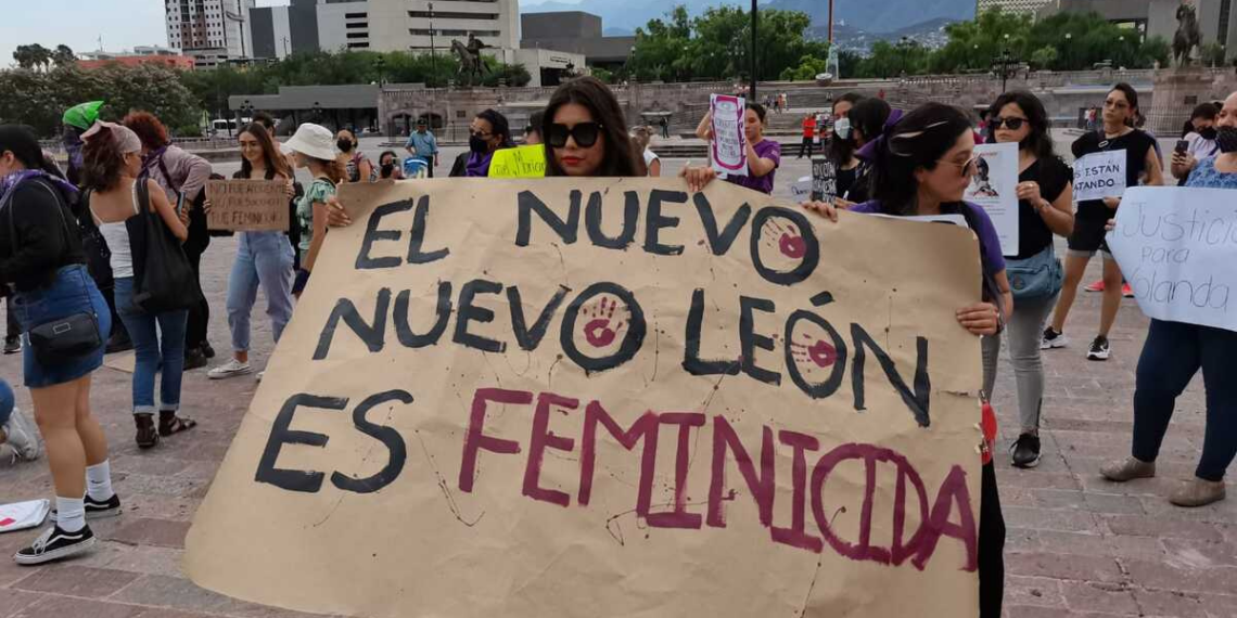 Feminicidios-desaparciones-nuevo-leon - Tu Colonia Regia Protesters Hold a Large Handwritten Banner That Reads 'el Nuevo León Es Feminicida' at a Demonstration, with People and Buildings in the Background. - Tu Colonia Regia
