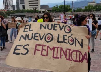 Protesters Hold a Large Handwritten Banner That Reads 'el Nuevo León Es Feminicida' at a Demonstration, with People and Buildings in the Background. - Tu Colonia Regia
